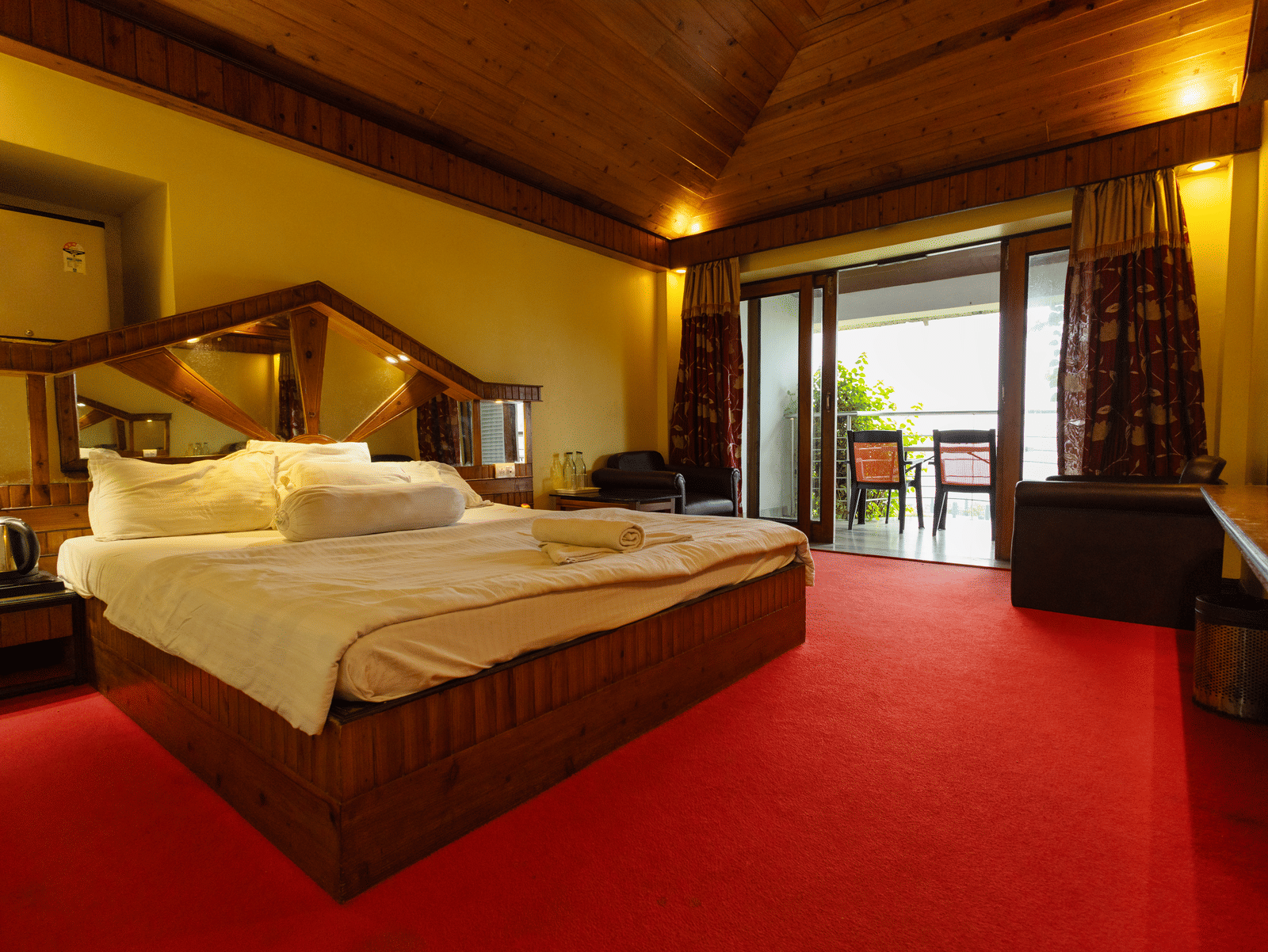 A bedroom with a king size bed, seating area, red carpet, and open balcony door at Hotel Seagull Digha.